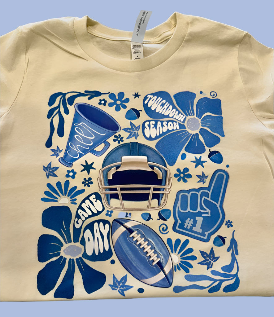 Beige t-shirt with blue football-themed graphics on a white background